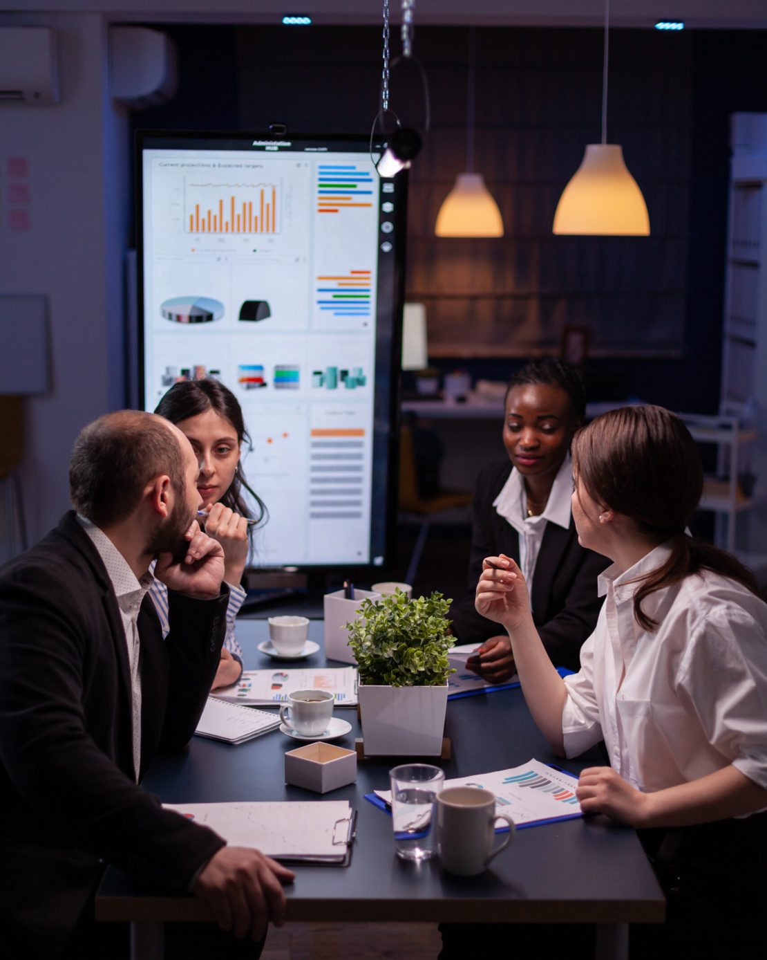 Workaholics businesspeople brainstorming financial company ideas analyzing strategy paperwork late at night in business office meeting room. Multi-ethnic coworkers checking solution